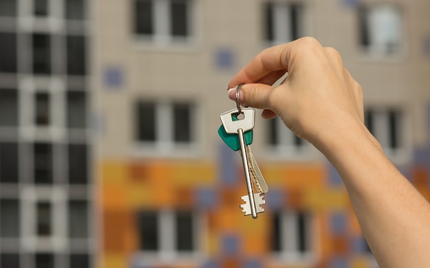 Close-up of apartment keys, new house in the background