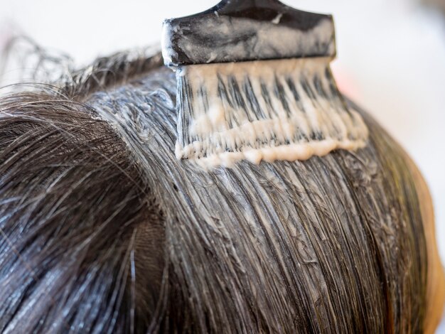 Foto primo piano dell'applicazione di vernice sui capelli delle donne con un pennello. cura dei capelli, colorazione dei capelli, parrucchiere, messa a fuoco selettiva