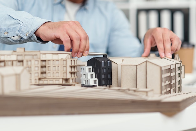 Close up architect's hands at constructing model of buildings and examines his work. Urban architecture and design concept.