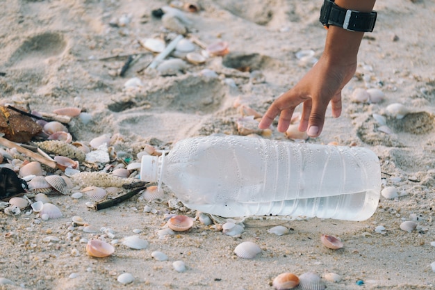 Close-up of arms children are picking up plastic bottles that\
are left on the beach.