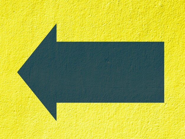 Photo close-up of arrow sign on yellow wall