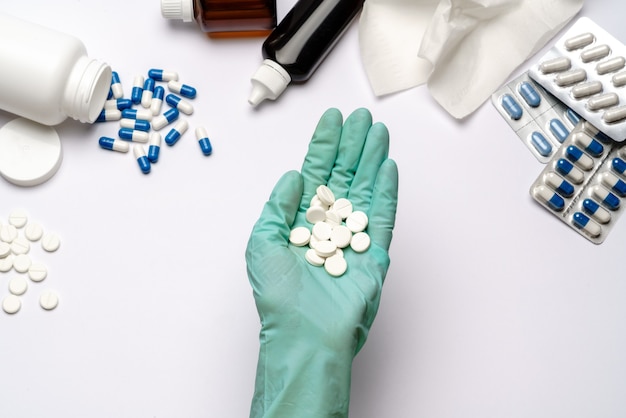 Close-up arts hand in een latex handschoen met tabletten over lichtgrijze of witte achtergrond met medische suppliements.