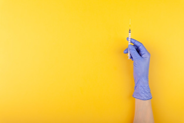 Close-up arts hand in medische handschoen met spuit op gele achtergrond