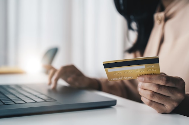 Close up of asian girl hold bank credit card and type on laptop shopping online using computer buying goods or ordering online entering bank accounts and details in online banking offer