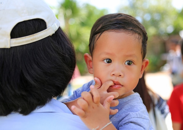 Close up asian mother carrying her son with sucking finger in mouth.