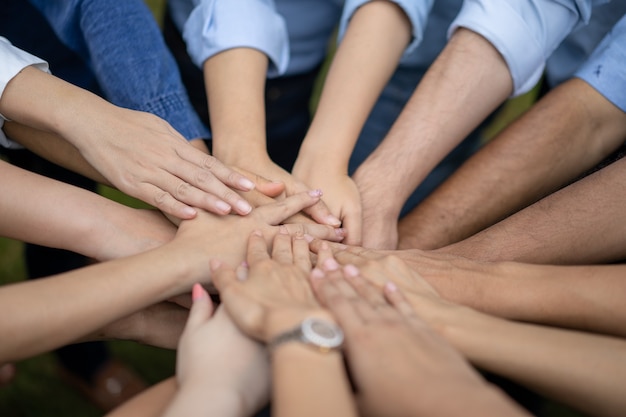 Photo close up to asian people hold hand together in the middle of their group, friend with stack of hand showing the love and community of good friends.