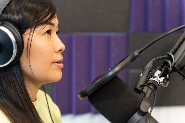 Close up of asian radio dj in headset working on a radio\
station. female radio working in front of microphone