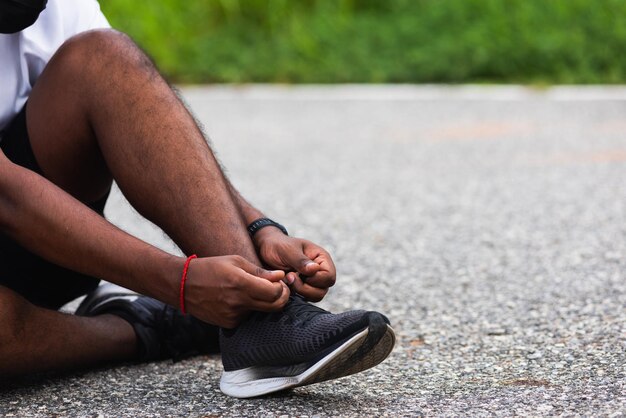 Close up Asian sport runner black man sitting shoelace trying running shoes getting ready for jogging and run at the outdoor street, health exercise workout concept