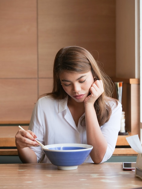 クローズアップアジアの女性退屈な顔レストランで麺を食べるための箸を使用しています。