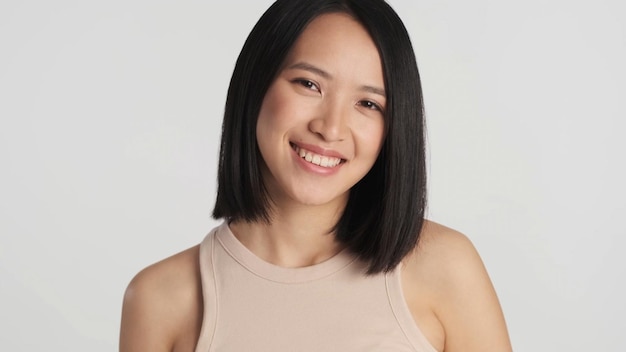 Close up Asian woman looking at camera over gray background Pretty Asian girl looking happy posing