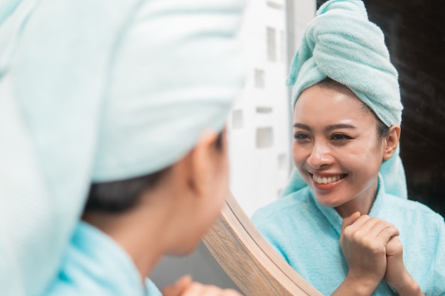 Азиатская женщина смотрит на отражение в зеркале после душа в ванной комнате крупным планом