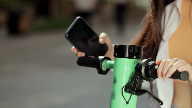 Foto la donna asiatica ravvicinata noleggia uno scooter elettrico utilizzando l'app per telefoni cellulari, un nuovo progetto di condivisione aziendale avviato nel trasporto ecologico della città city