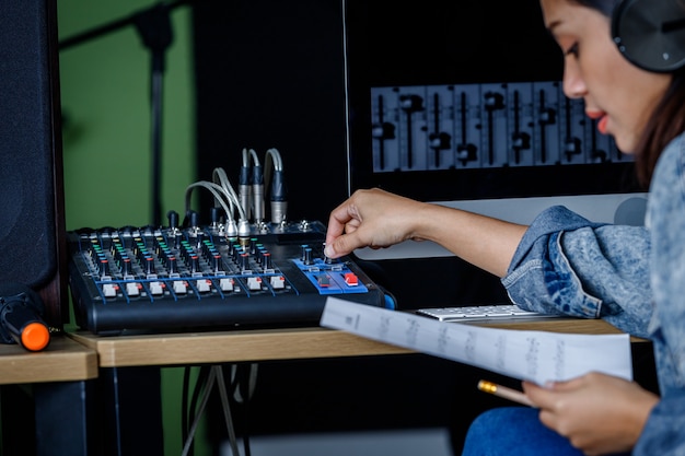 Foto primo piano del cantante donna asiatica che indossa le cuffie che registra una canzone davanti all'attrezzatura del banco di controllo per la registrazione del suono in uno studio professionale