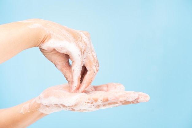 Foto primo piano di donne asiatiche pulizia delle mani con bolle di sapone bianche su sfondo blu. dimostrazione di lavaggio delle mani per la protezione dai virus. concetti di igiene e prevenzione del covid 19