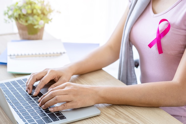 Close up of asian women disease mammary cancer patient with pink ribbon wearing headscarf After treatment to chemotherapy with working business at laptop in office at home,medicine concept