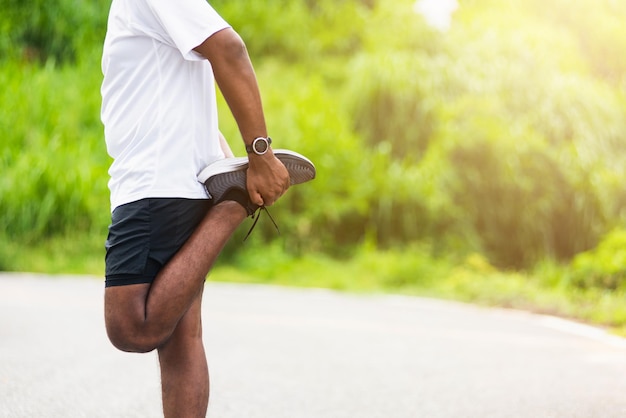 Крупным планом азиатский молодой спортсмен спортивный бегун темнокожий мужчина носит часы, поднимает ноги, растягивает ноги и колено перед бегом в парке здоровья на улице, здоровые упражнения перед концепцией тренировки