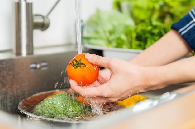 Close up asian young woman washing tomato broccoli carrot fresh vegetables paprika with splash water in basin of water on sink in kitchen preparing fresh salad cooking meal Healthy food people