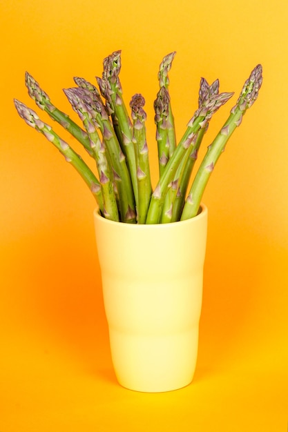 Close-up of asparagus in drinking glass over yellow background