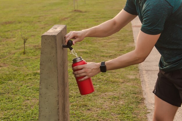 公共の水飲み場から彼のホッピーで水を運ぶ運動選手のクローズアップ。