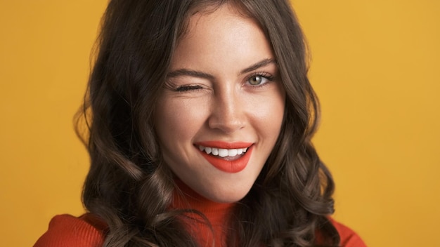 Close up attractive flirty brunette girl with red lips winking on camera over colorful background