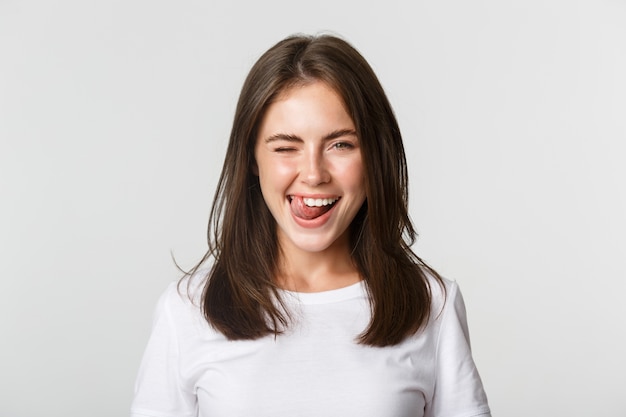 Close-up of attractive happy young woman winking joyfully and showing tongue sassy.