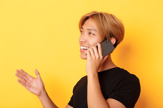 Photo close-up of attractive korean guy smiling and talking on mobile phone happy