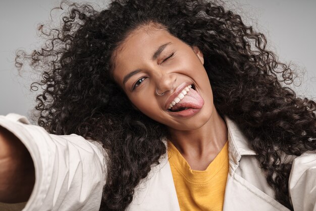 Primo piano di un'attraente giovane donna africana sorridente con i capelli ricci, che indossa un cappotto autunnale