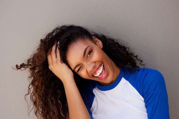 Close up attractive young black woman smiling with hand in hair against gray wall