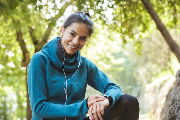 Close up of an attractive young fitness woman wearing sportswear exercising outdoors, using smartwatch