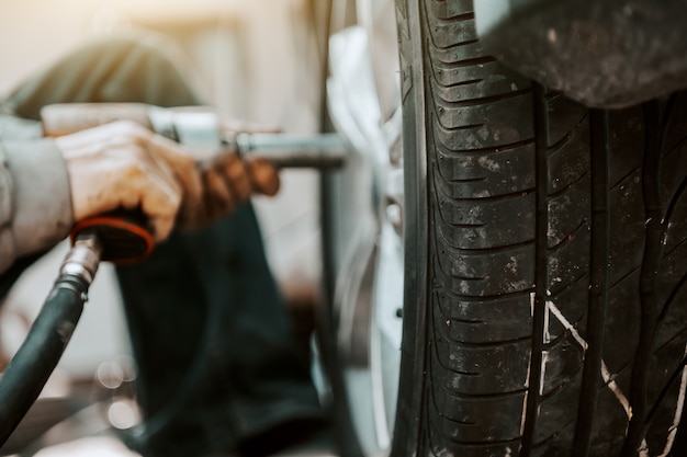 Close up of auto mechanic using tool to change tire while crouching at workshop.