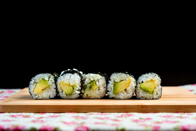 close-up of avocado sushi arranged on cutting board against black background