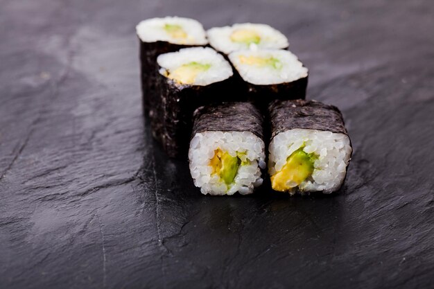 Close-up of avocado sushi roll set on a black slate background