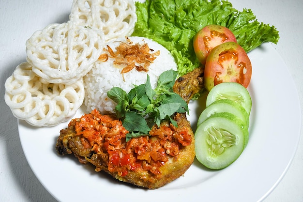 Крупный план индонезийской еды аям гепрек с острым соусом чили самбал, подаваемым рисом на белой тарелке