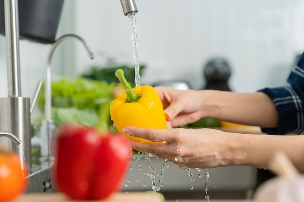 Close-up aziatische jonge huishoudster vrouw wassen paprika gele paprika groenten met splash water in bekken op gootsteen in keuken voorbereiding van verse salade koken maaltijd gezonde voeding mensen