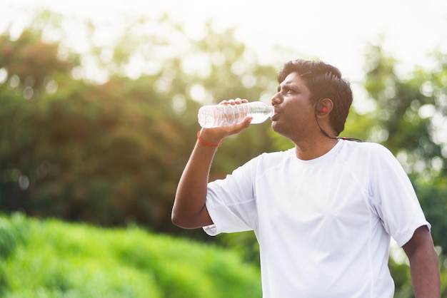 Close-up Aziatische jonge sport runner zwarte man draagt atleet koptelefoon hij drinkt water uit een fles na het hardlopen in het outdoor street health park, gezonde oefening training concept