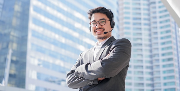 Close-up aziatische man callcenter agent draagt een headset en glimlacht naar buiten kantoor over vervagen stad gebouw achtergrond voor toekomstige telemarketing en helpdesk concept