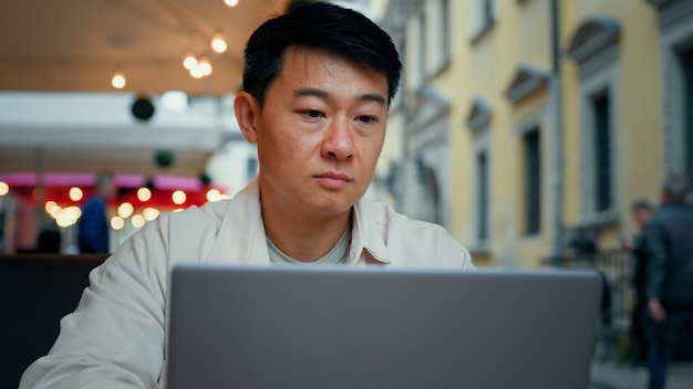 Close-up aziatische man zittend in café typen op laptop online chatten goed bericht mannelijke toerist lezen