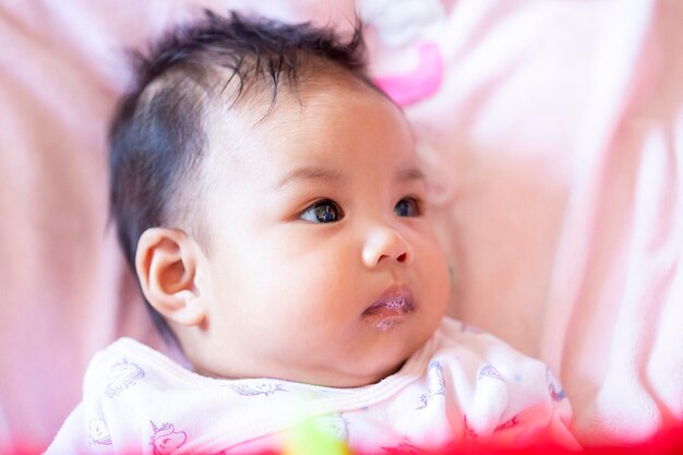 Photo close-up of baby girl looking away while lying on bed