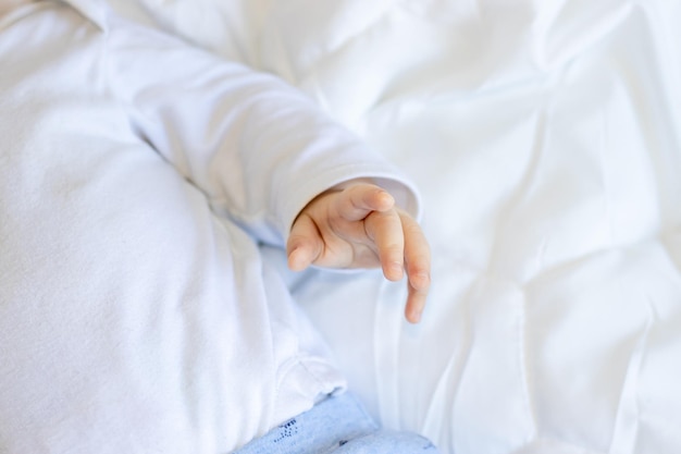 close up of baby little hand on white soft blanket toddler in white bodysuit and blue pants