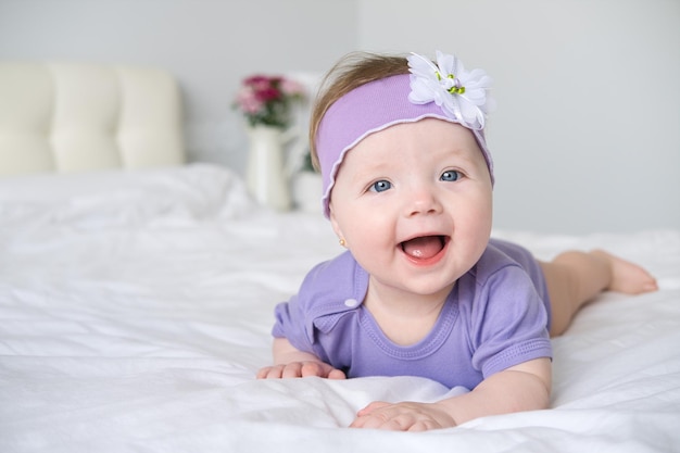 close up baby with blue eyes wearing a purple outfit smiling lying on bed