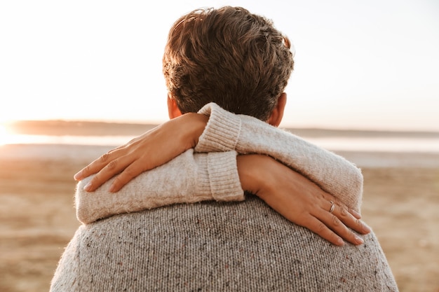 Close up back view of a beautiful young couple standing at the sunny beach, embracing