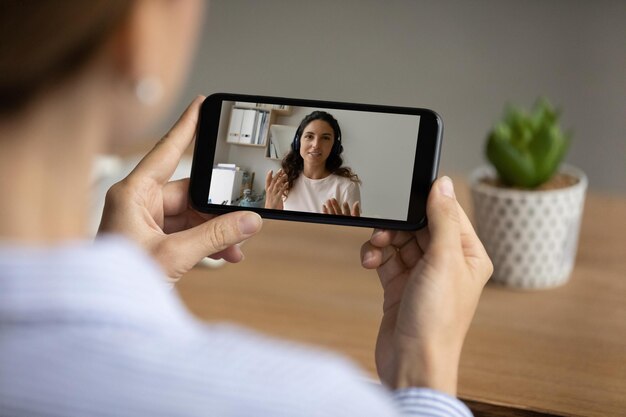 Close up back view of female watch online lesson or coach\
webinar on cellphone gadget woman talk speak on video call with\
colleague have webcam digital conference or virtual event on\
smartphone