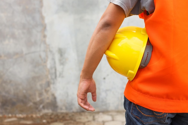 Photo close up back view of male construction worker wearing orange vest and holding safety helmet outdoo