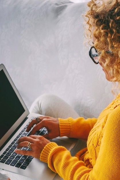 Close up back above view of woman writing on laptop sitting on bed Modern people using computer at home in indoor leisure activity Vertical female working on notebook alone at home Concept online