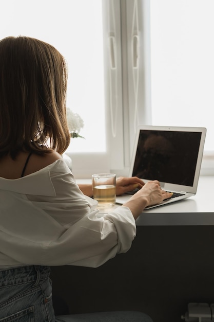 Close up of back view young pretty concentrated woman typing and browsing online on laptop working on computer while sitting in cozy room alone Distance learning and work concept