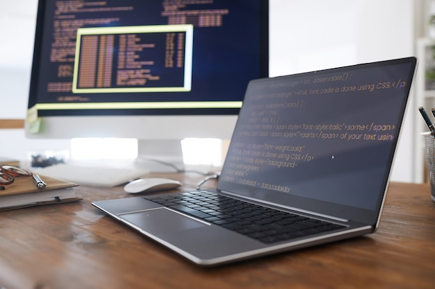 Фото Закройте фоновое изображение черного и оранжевого программного кода на экране компьютера и ноутбука в современном интерьере офиса, скопируйте пространство
