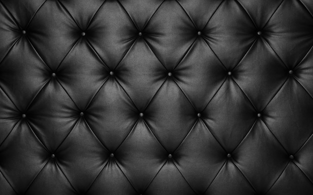 Photo close up background texture of black capitone genuine leather, retro chesterfield style soft tufted furniture upholstery with deep diamond pattern and buttons