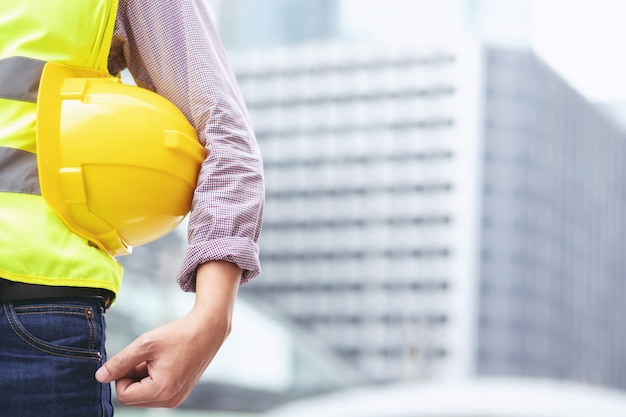 Foto chiuda sulla vista posteriore dell'operaio edile maschio di ingegneria che tiene il casco giallo di sicurezza e indossa indumenti riflettenti per la sicurezza dell'operazione di lavoro.