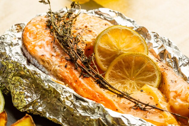 Close up of baked fish slice in foil with branch of thyme and lemon slices on the top