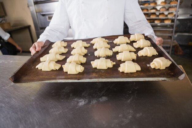 Close up of baker holding tray of raw dough